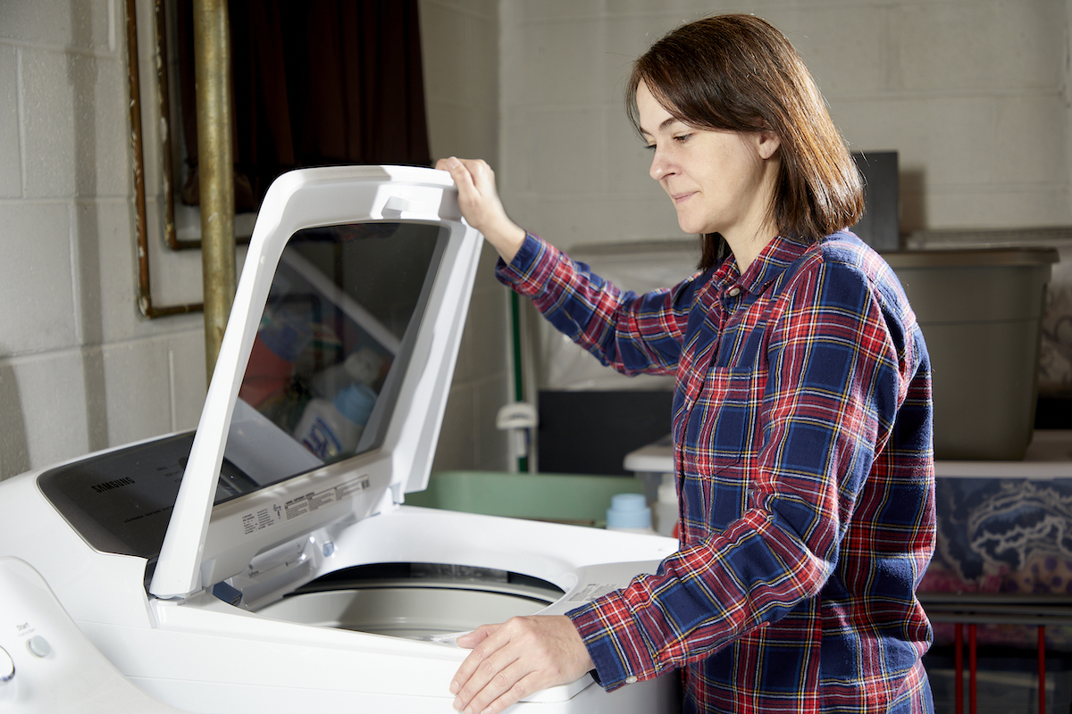 Woman looks puzzled as she looks into top-load washing machine.