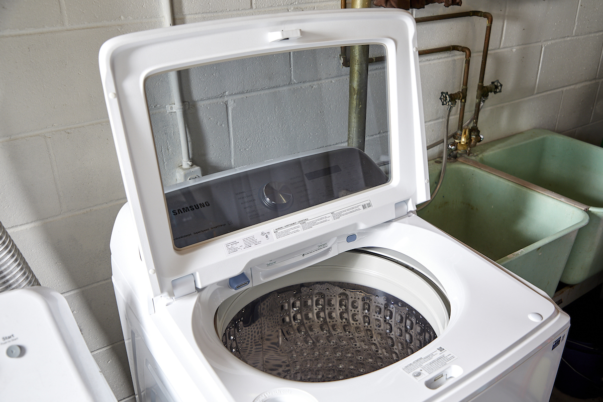 A white top-load washing machine with the top open, next to a green utility sink.