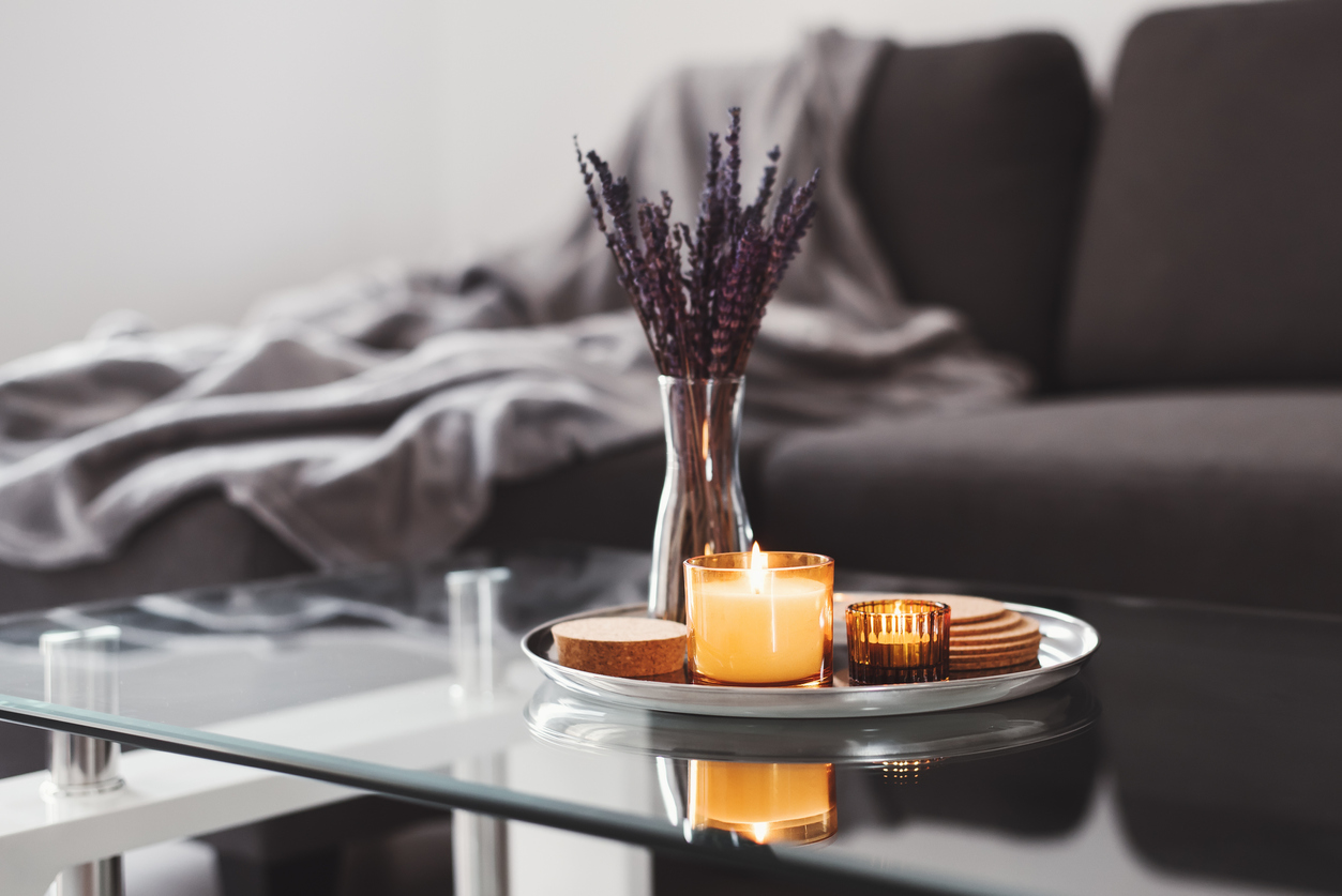 Lit candle on a tray with other decor on top of a glass coffee table.