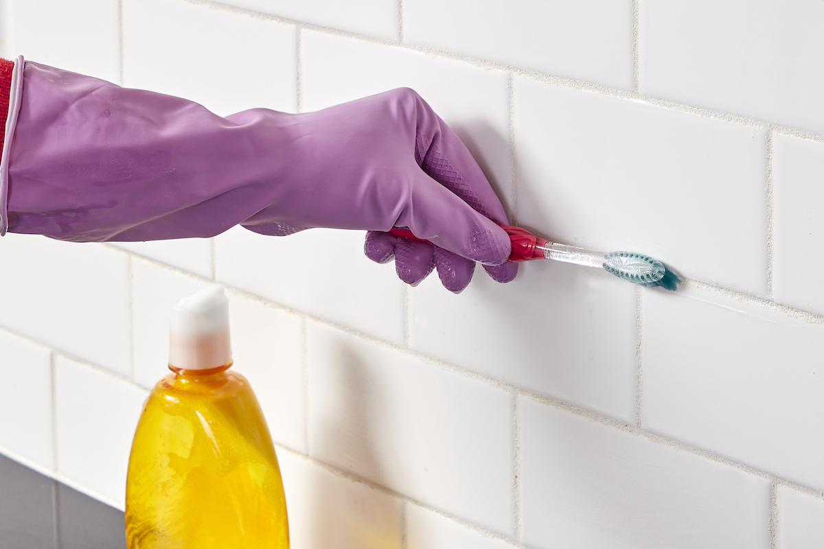 Woman uses toothbrush to apply homemade grout cleaner to tile grout.