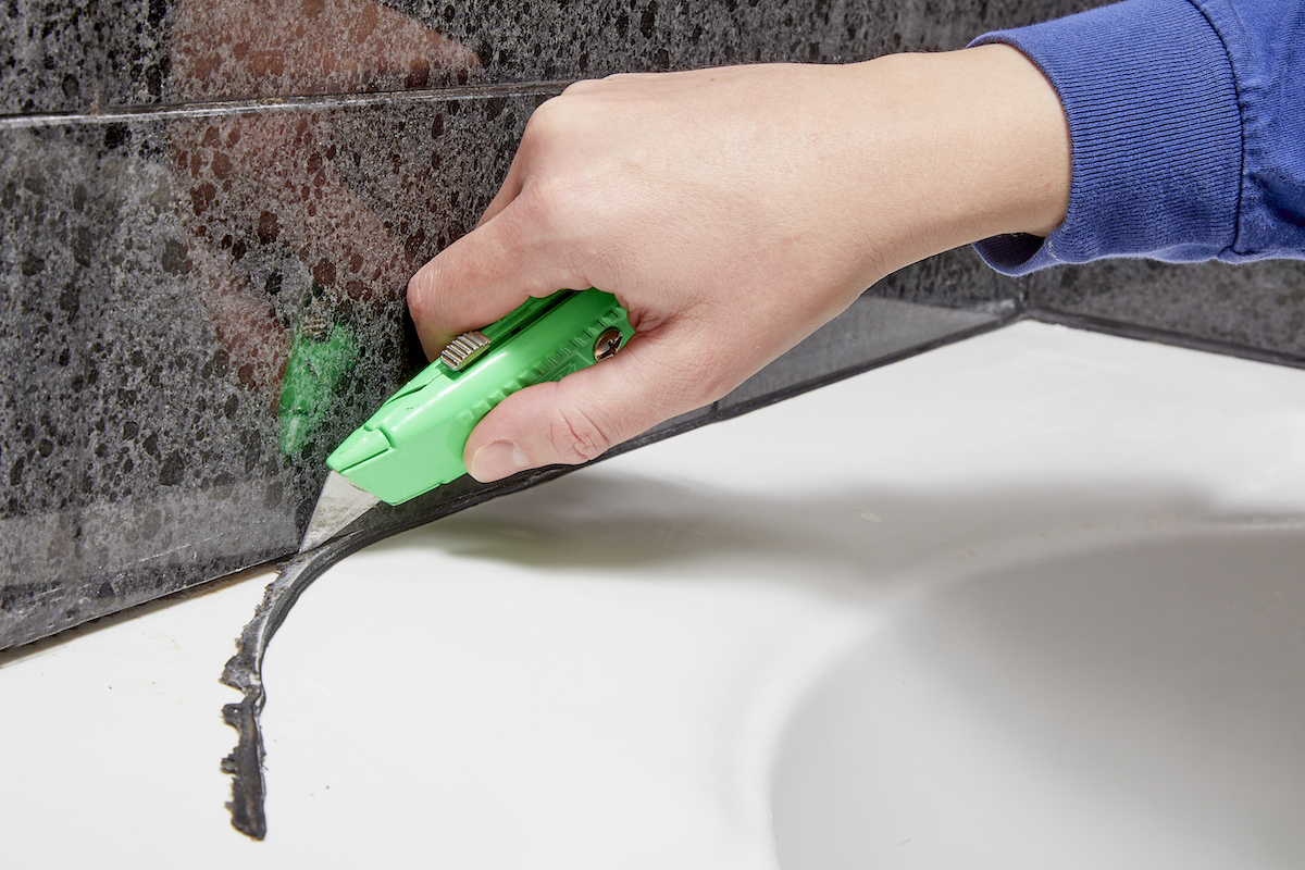 Woman uses a utility knife to remove caulking around her bathtub.