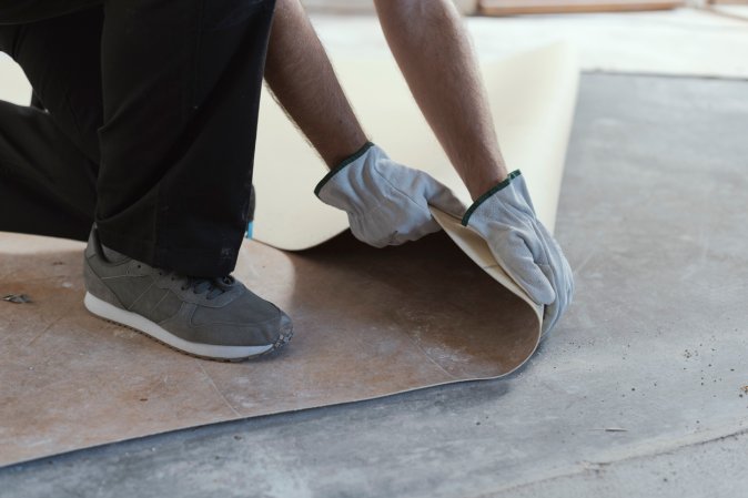 Person wearing gloves rips up vinyl flooring.