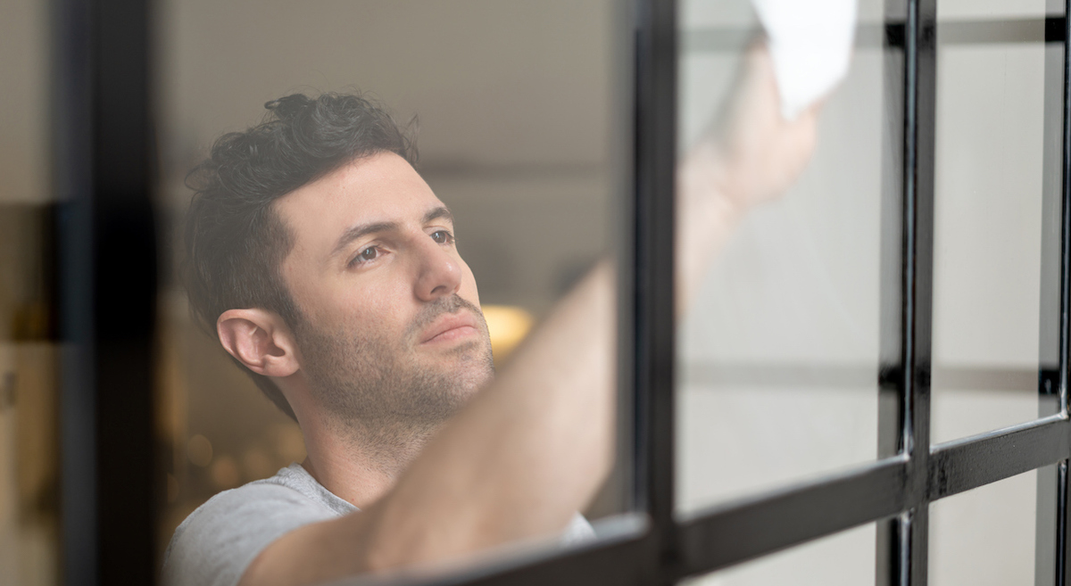 Handsome young man indoors cleaning a black-paned window.