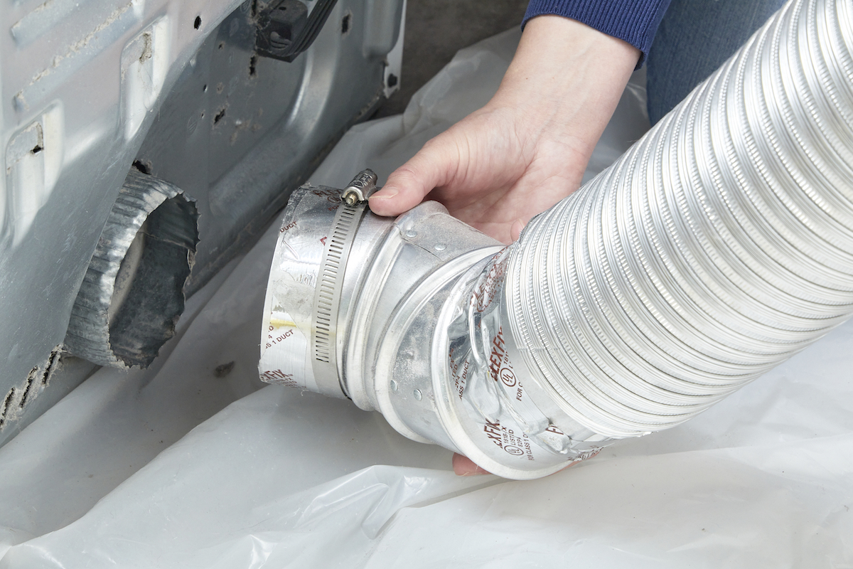 Woman disconnecting dryer vent hose from the back of her dryer.