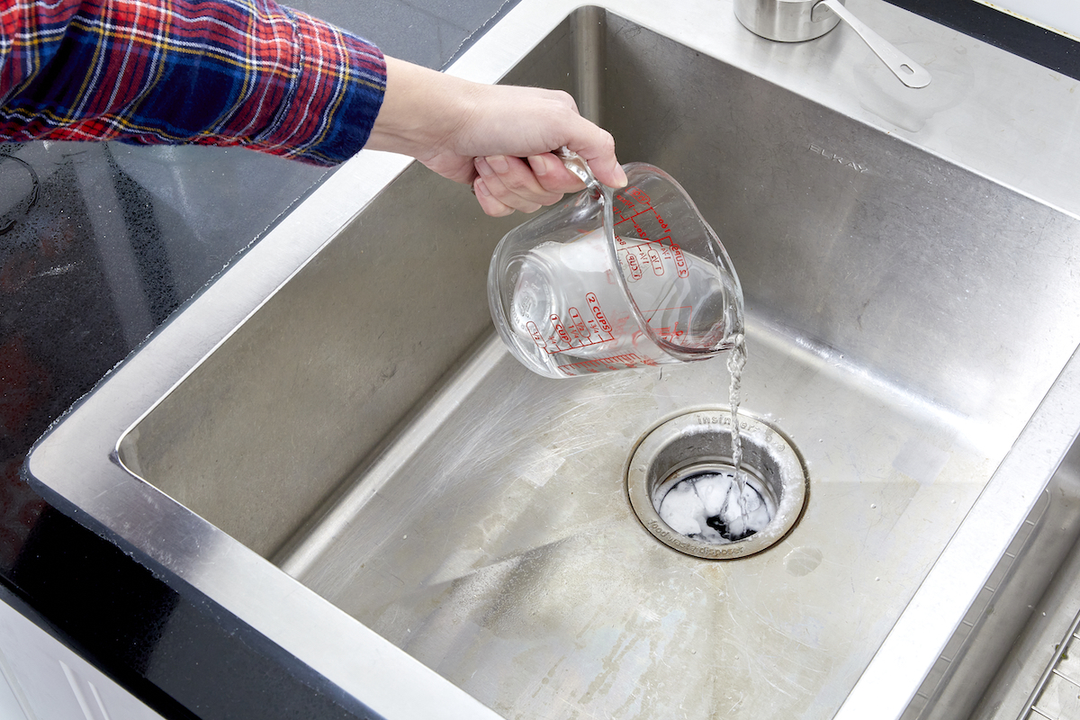 Woman pours vinegar and baking soda down the garbage disposal.