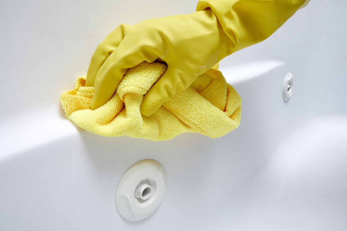 Person wearing yellow rubber gloves uses yellow microfiber cloth to clean jetted tub.