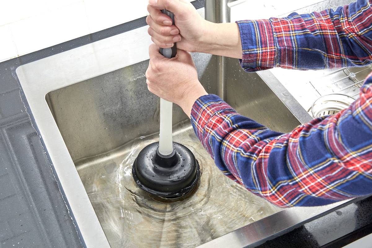 Woman uses plunger to clear a sink drain.