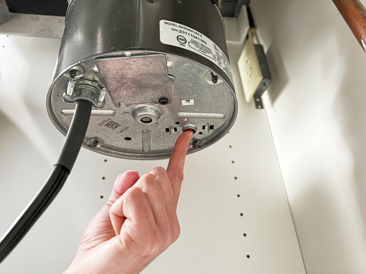 Person pushes the reset button on the underside of a garbage disposal.