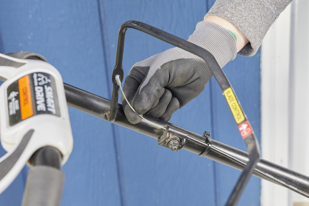 Woman pulls on flywheel brake near lawn mower handle.