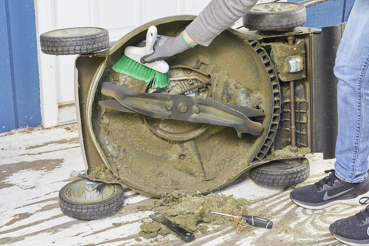 Woman turns lawn mower over to access and clean the deck.