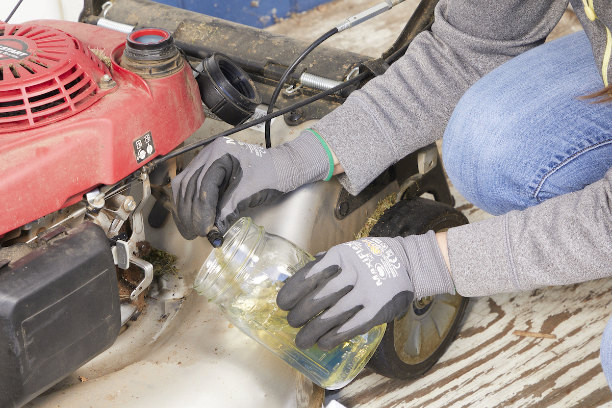 Woman drains old gas from a lawn mower into a mason jar.