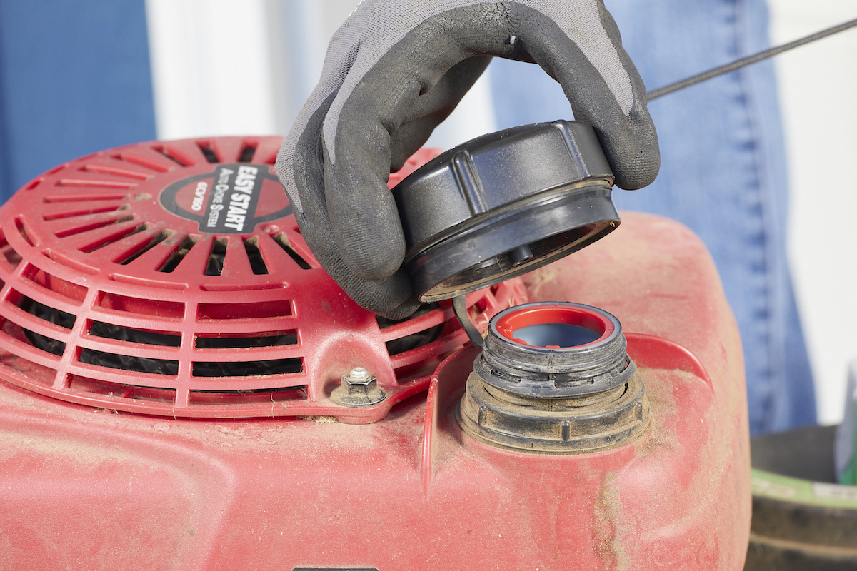 Woman opens the fuel tank on her lawn mower.