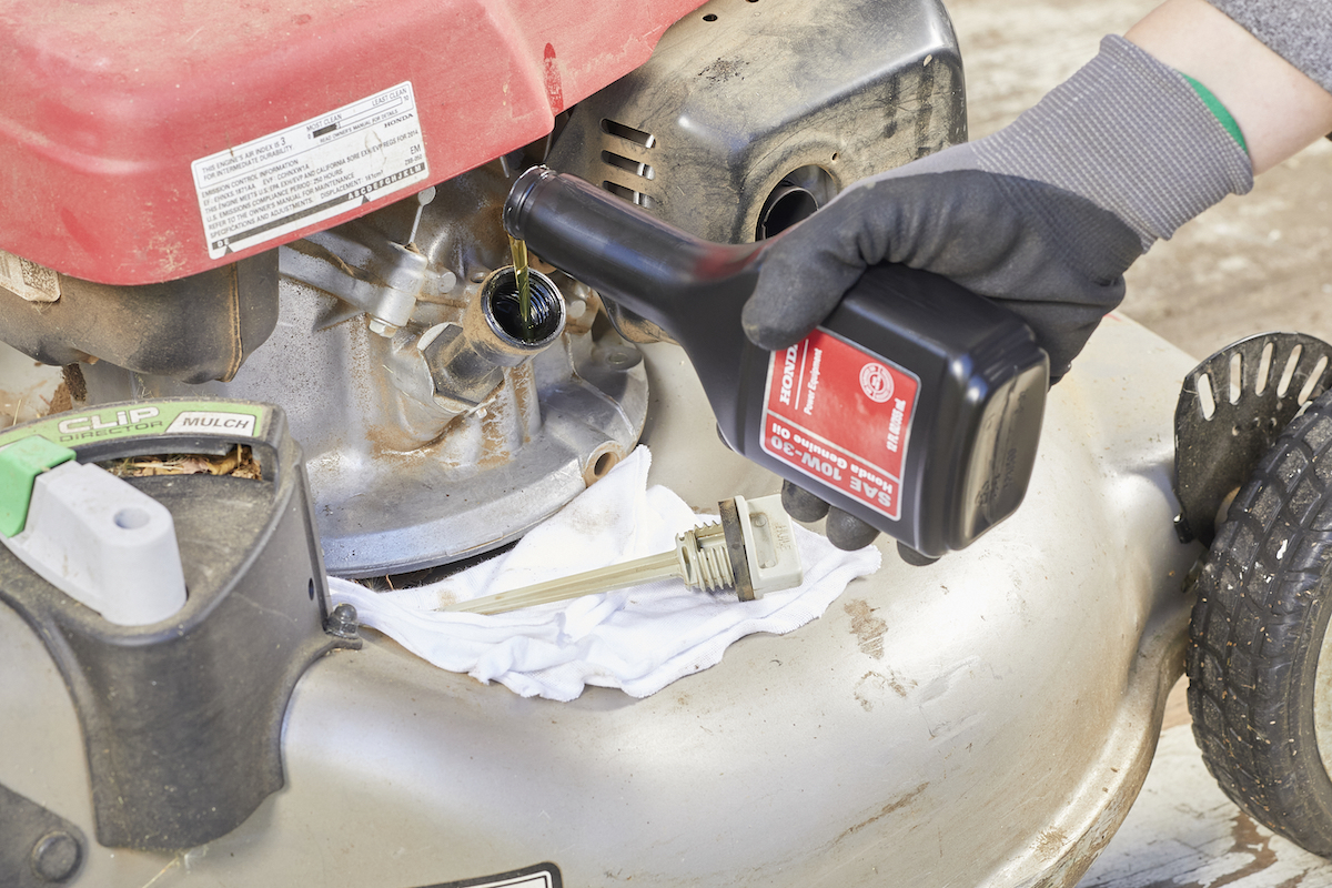 Woman wearing work gloves pours motor oil into a lawn mower.