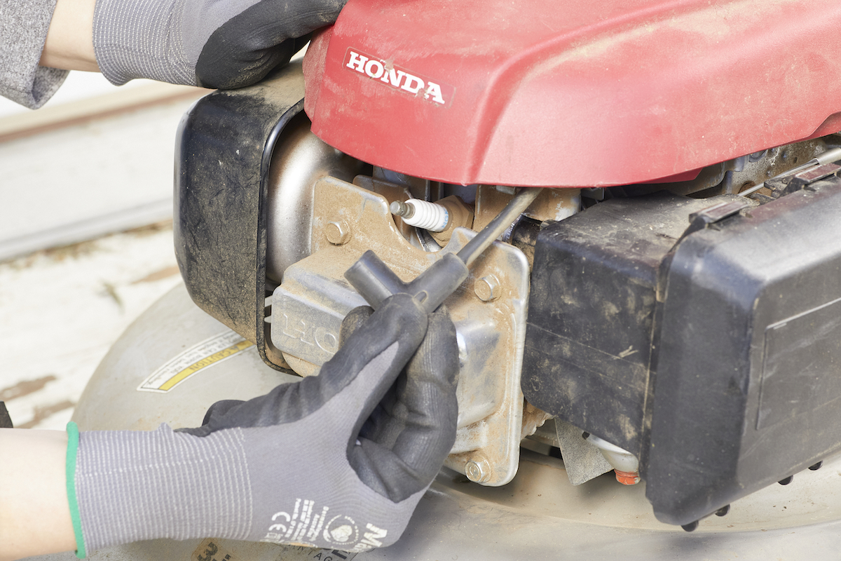 Woman inspects safety release mechanism cable by engine on lawn mower.