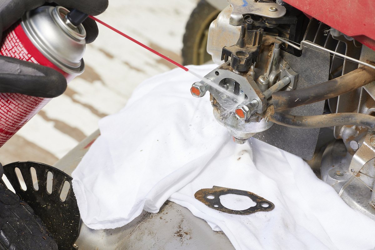 Woman sprays aerosol spray with narrow nozzle onto plugs in lawn mower.