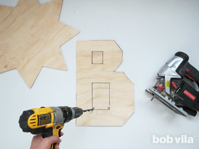 Person creating a pilot hole in plywood using a drill for a jigsaw to later cut the holes of the letter B.