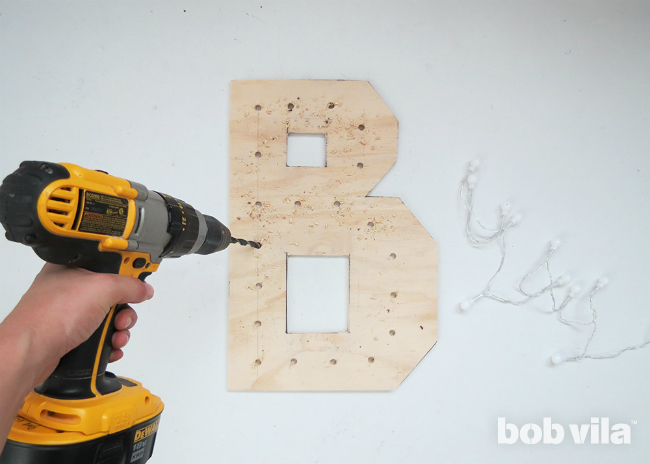 A DIYer drills holes into the letter B where each light bulb will be placed.