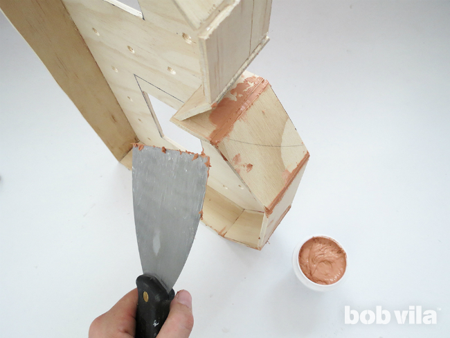 A DIYer uses woody putty  to fill in any gaps on the plywood marquee letter.