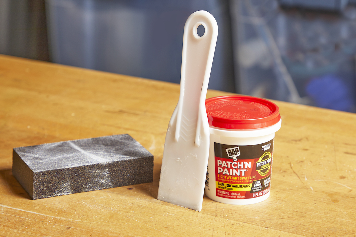 Materials needed to spackle a wall: sanding block, putty knife, and spackle.