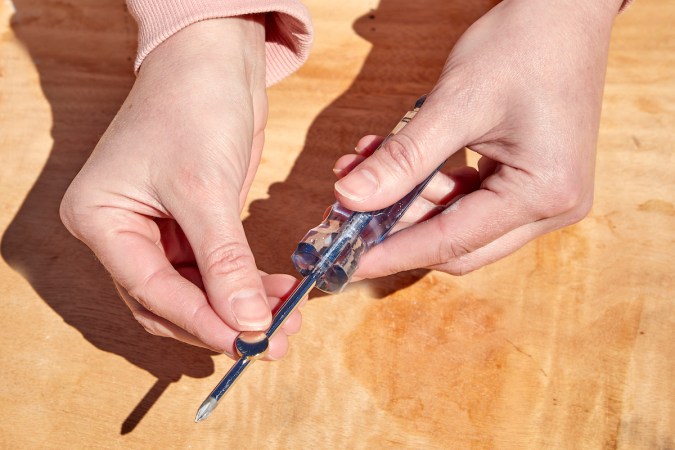 Woman slides neodymium magnet along the shaft of a screwdriver to magnetize it.