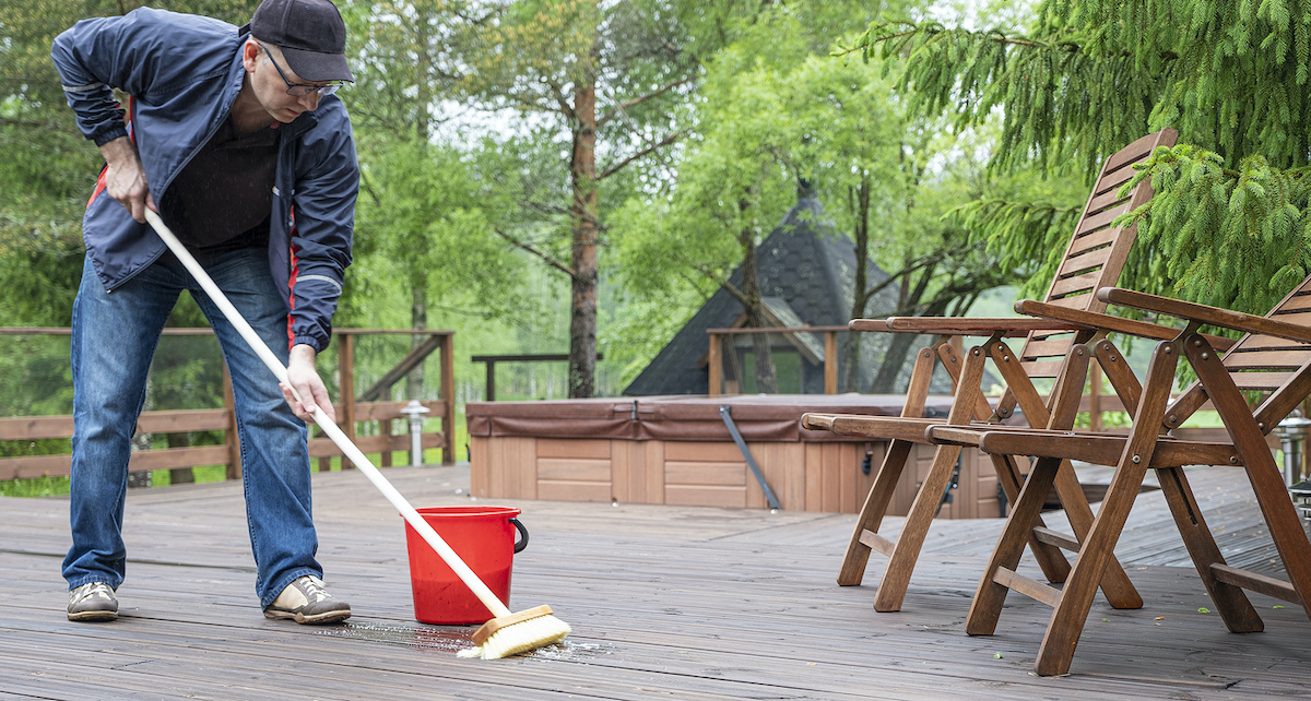 A man is using a long brush to scrub a deck clean.