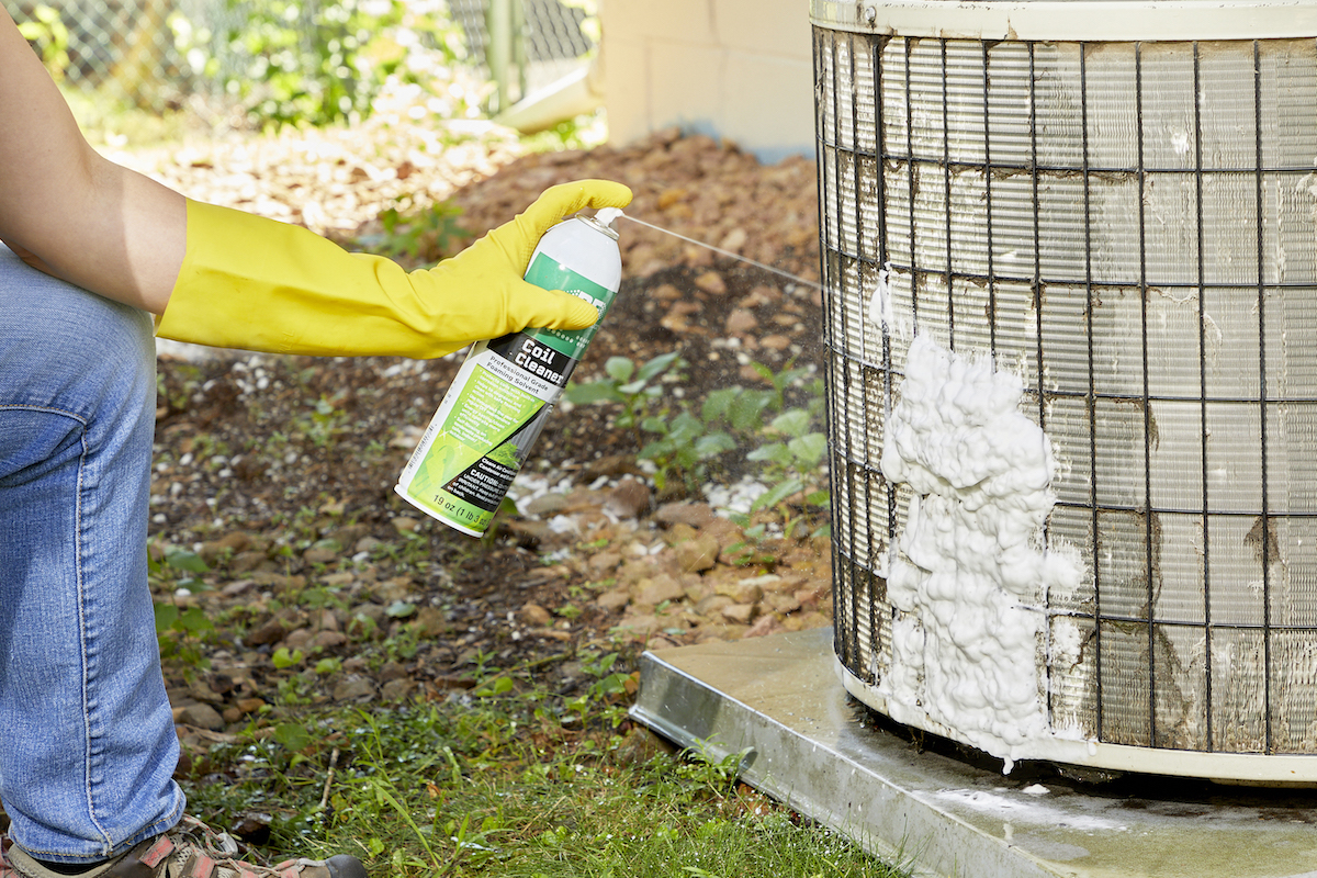 Woman sprays foam coil cleaner onto AC coils.