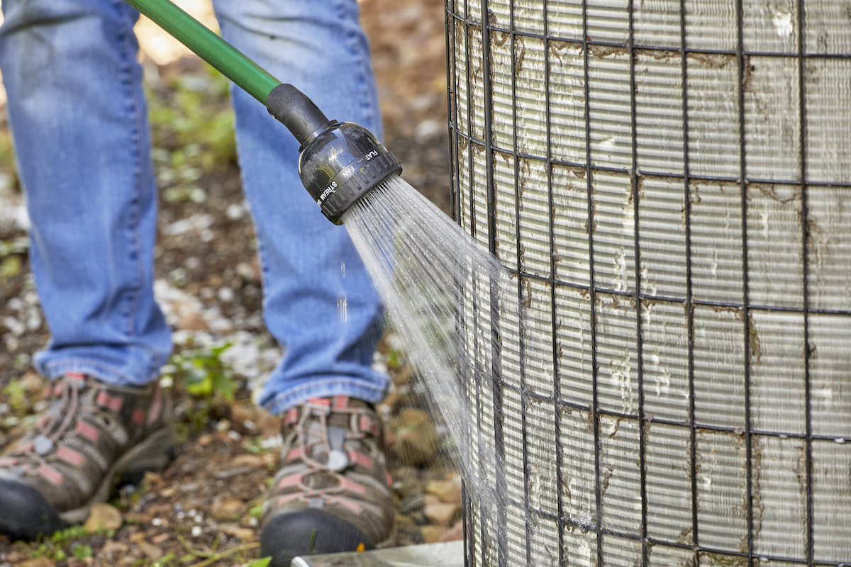 Woman uses a garden hose to rinse AC coils.