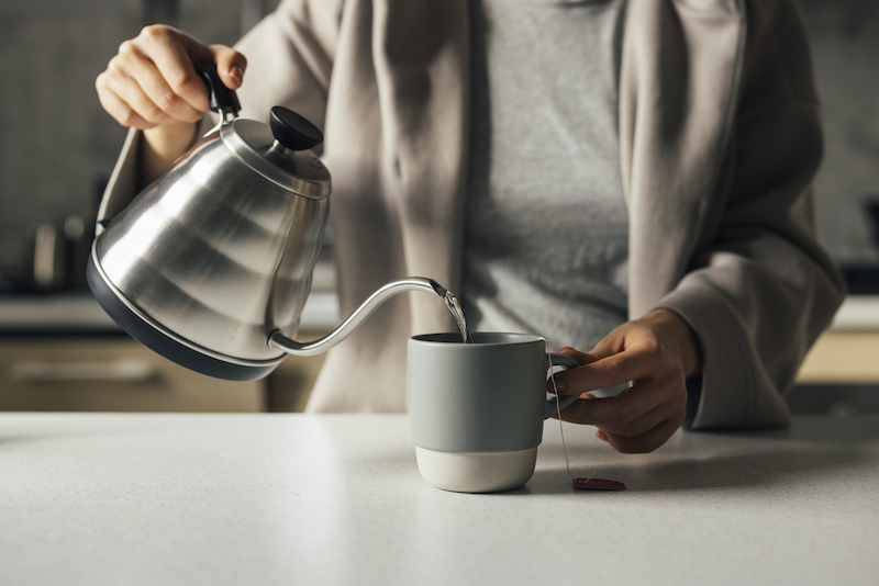 unrecognizable woman pouring water into teacup