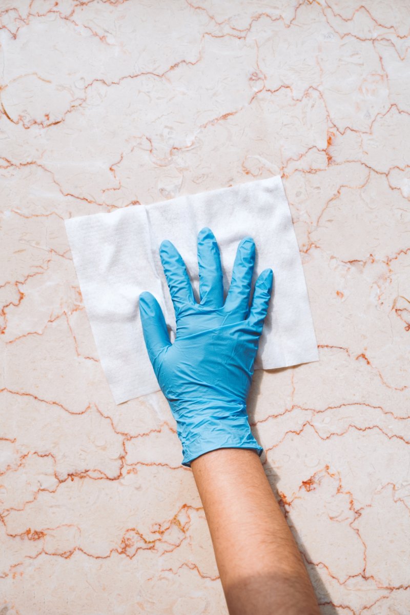 A gloved hand using a white towel to wipe marble table.