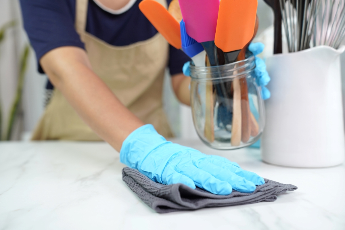 A person wearing gloves is cleaning under kitchen utensil holders.