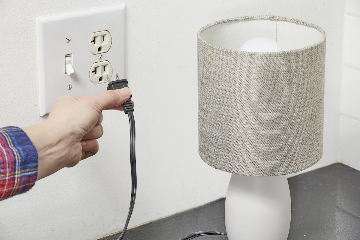 Woman plugs a small desk lamp into a kitchen outlet.