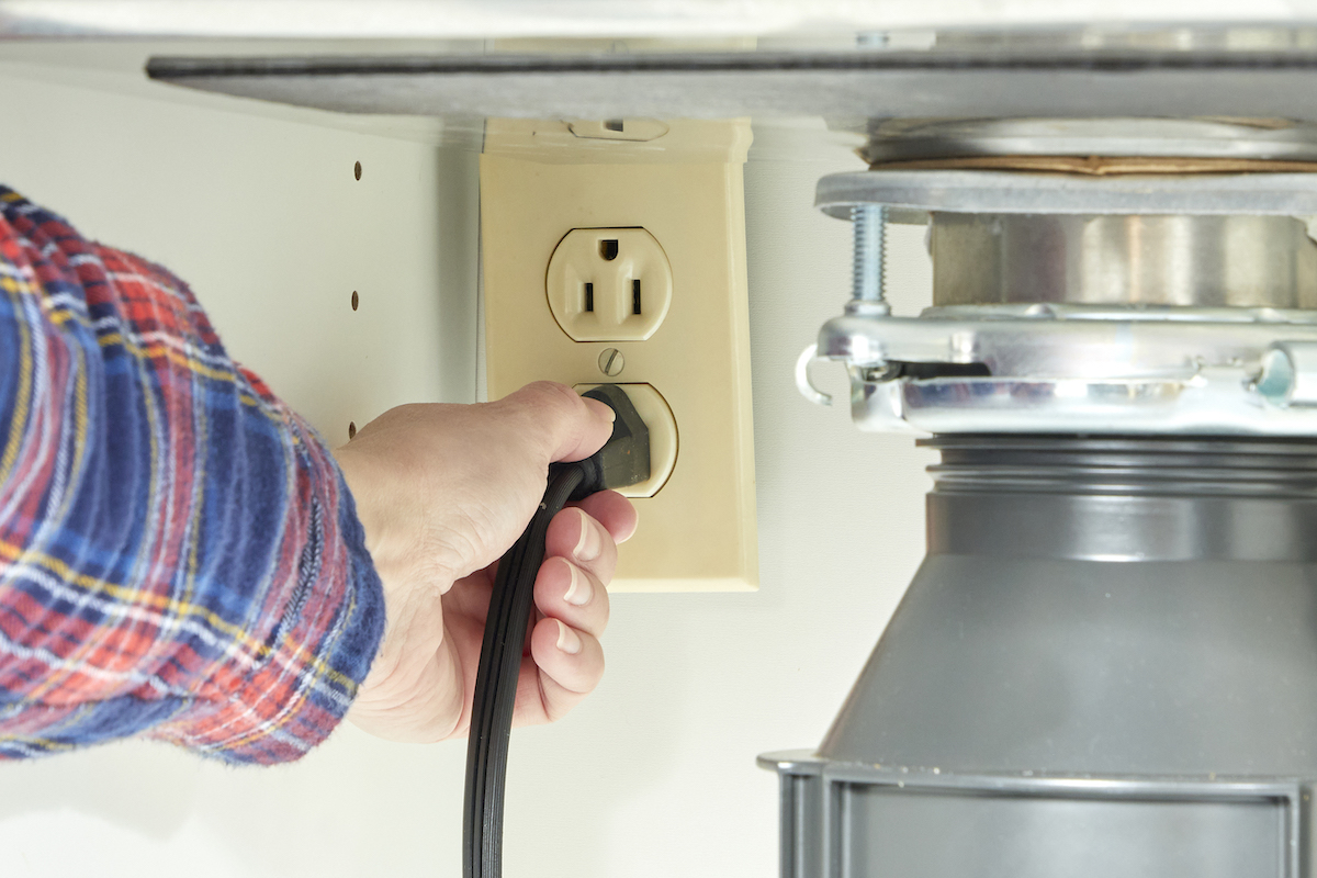 Person plugs in a garbage disposal under a kitchen sink.