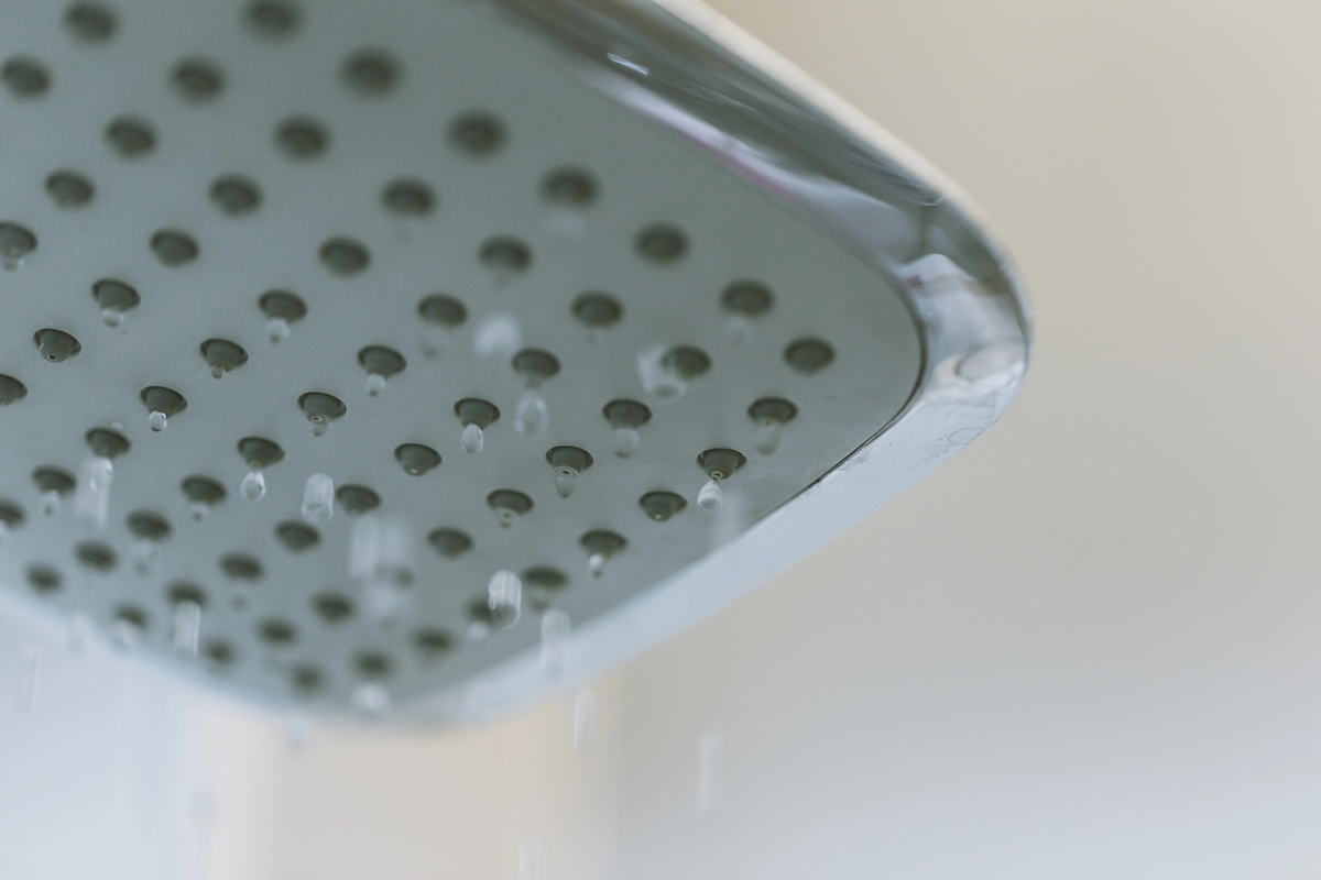 A shower head is demonstrating low water pressure against white tile.