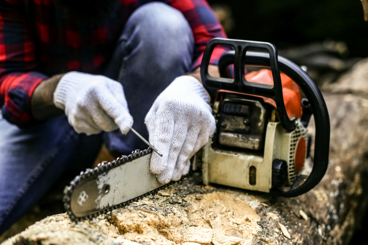 A gloved lumberjack is using a tool to sharpen his chainsaw.