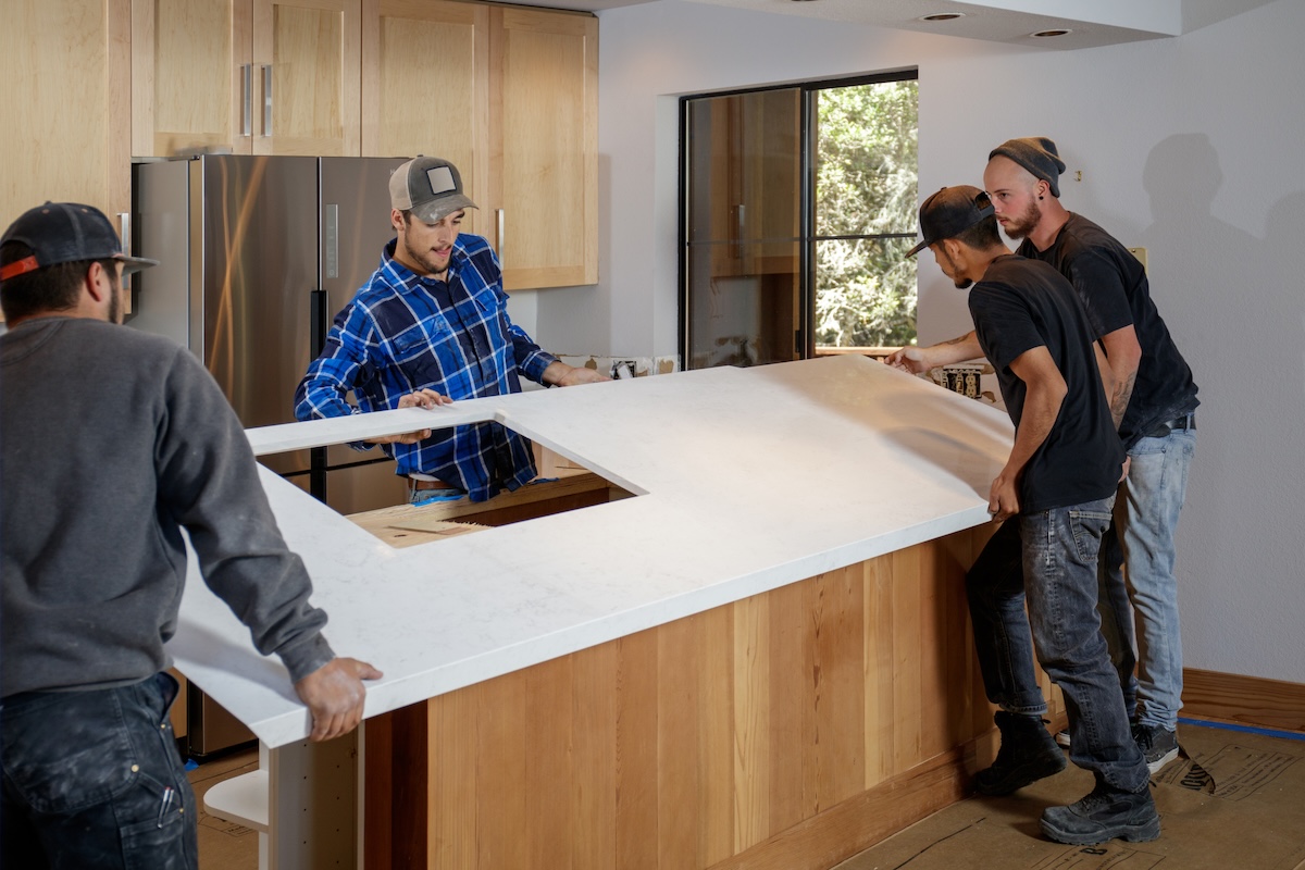 Contractors installing a quartz countertop in a kitchen.