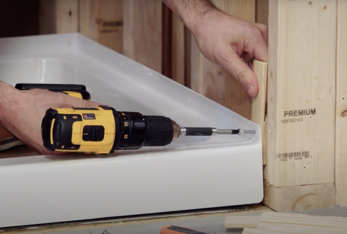 Person is using a drill to screw shower pan into a wall stud.