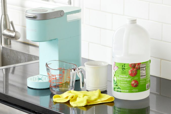 Ice blue Keurig machine on a counter with rubber gloves, vinegar, and other cleaning supplies.