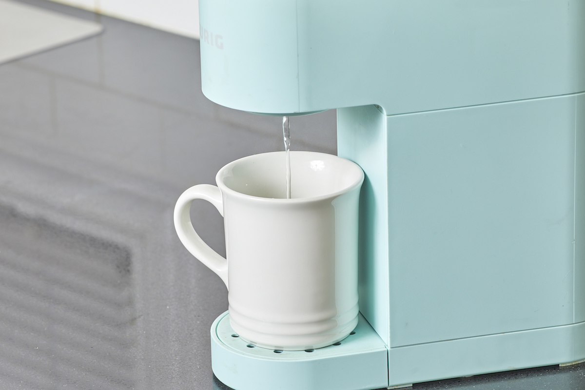 Cleaning solution drips through a Keurig machine into a white mug.