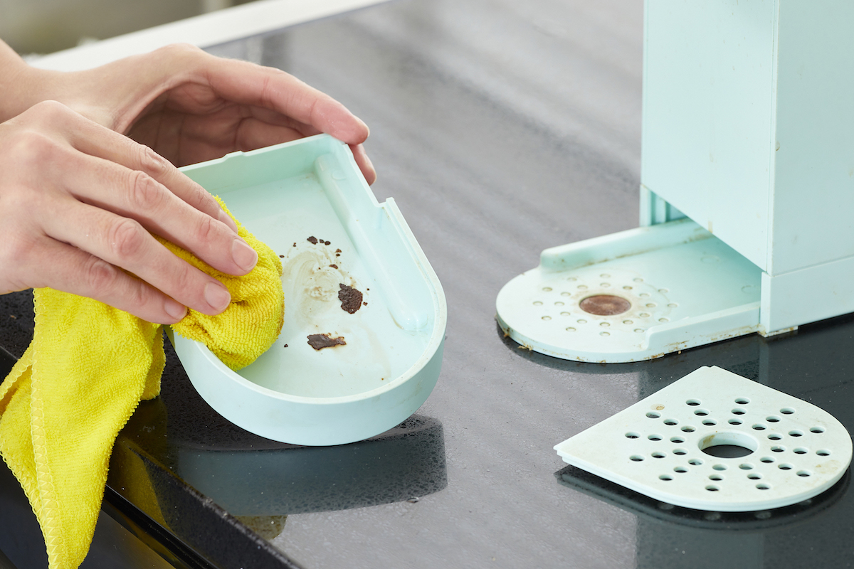 Woman cleans the base parts of an ice blue Keurig that has been disassembled.