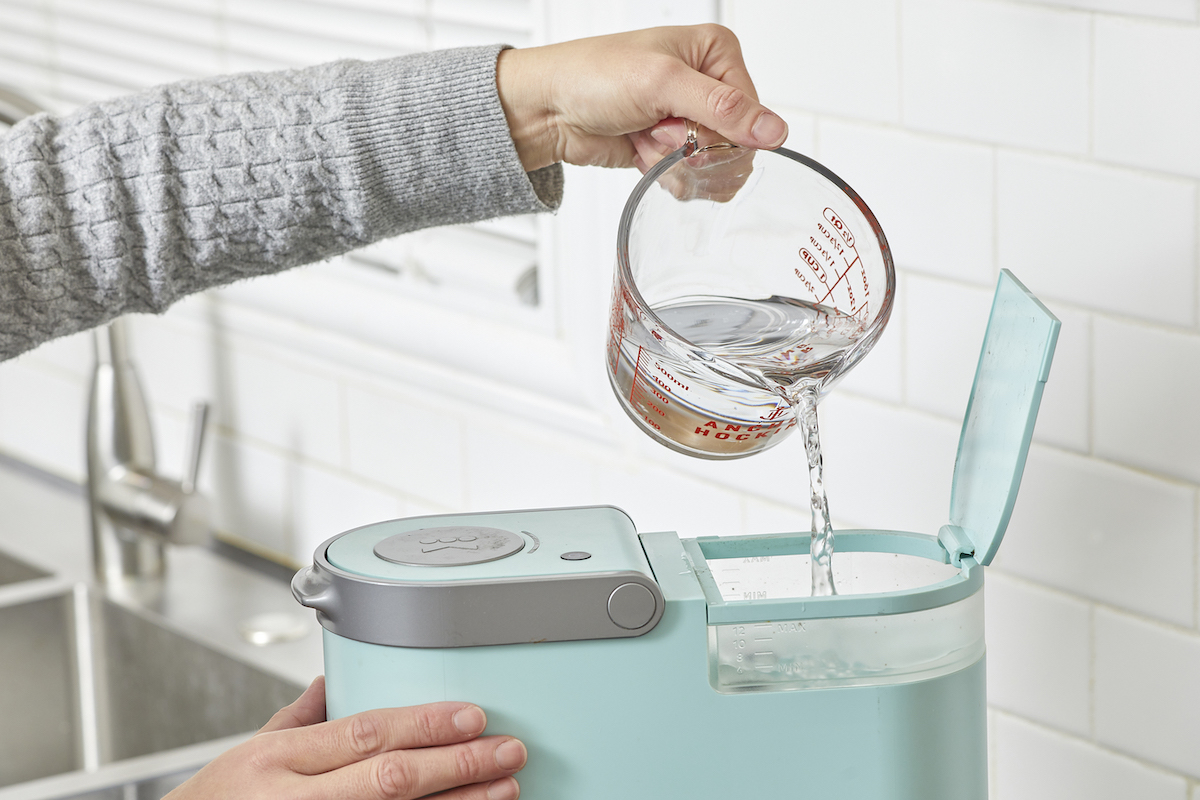 Woman pours a measuring cup of vinegar solution into a Keurig.