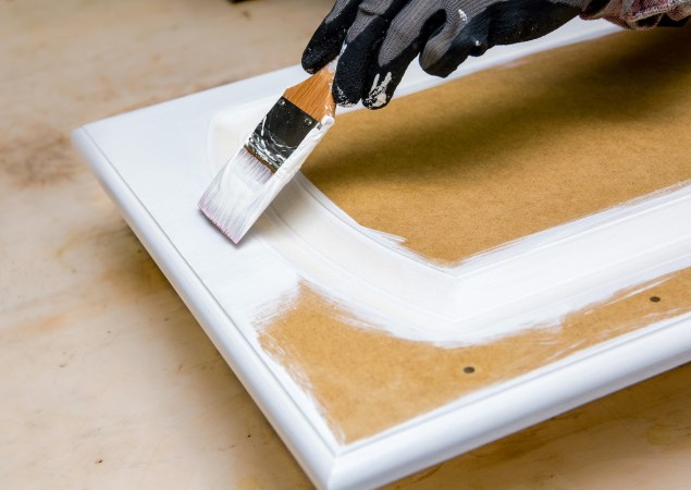 A person is painting a kitchen cabinet door made of MDF with white paint with a brush.