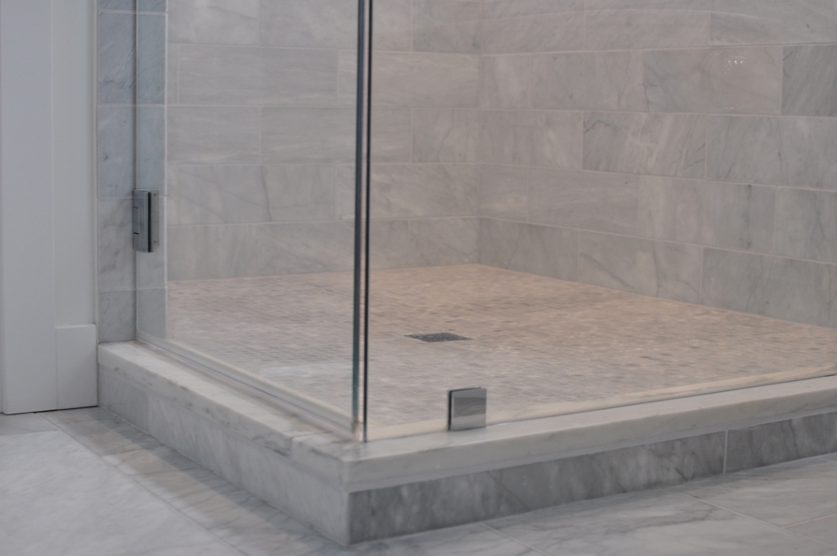 Bathroom shower with tile floor, and glass wall surrounds.