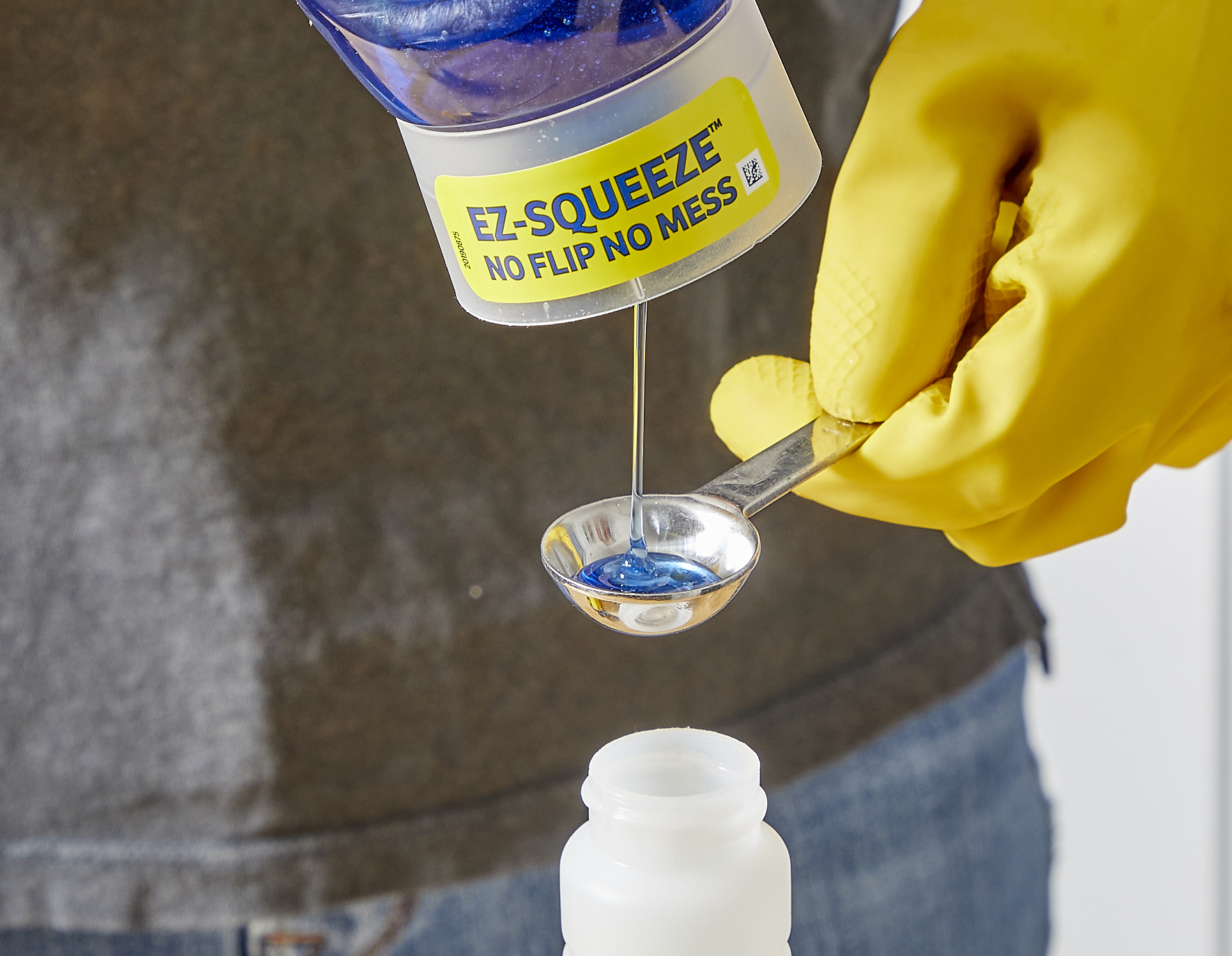 Woman measures dish soap into a measuring spoon above a spray bottle.