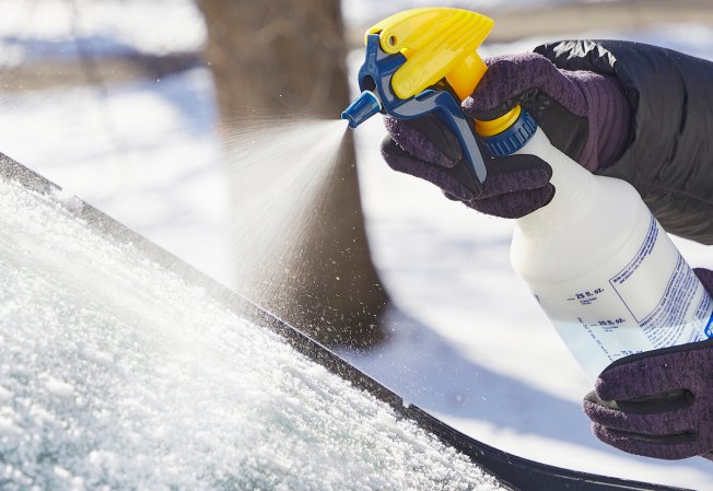 Person sprays de-icer onto a frosty car windshield.