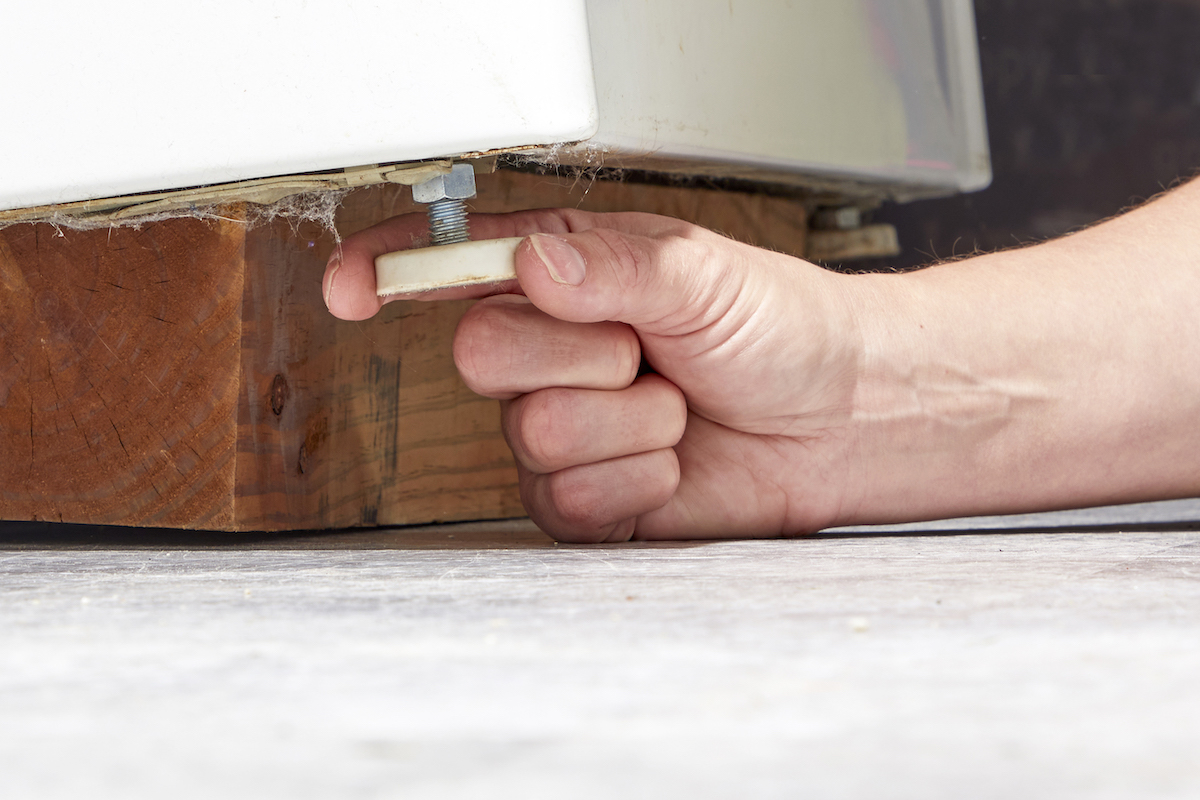 Woman adjusts footings underneath clothes washer to level the machine.