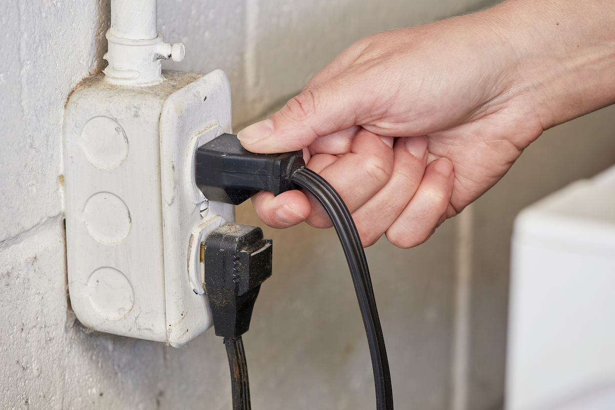 Woman checks plugs in a basement outlet to make sure they are properly inserted.