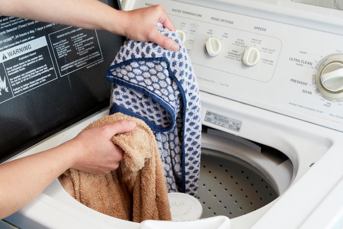 Woman rearranges towels in a top-load washing machine.