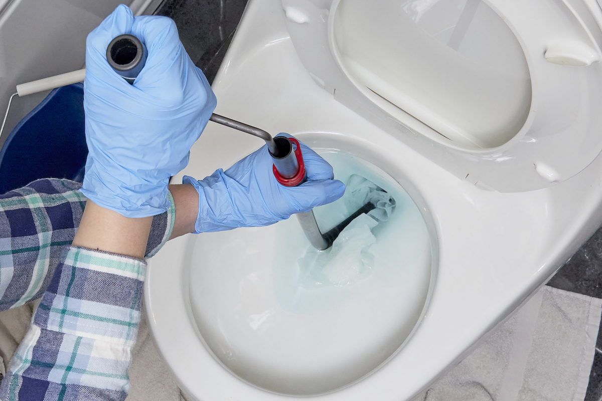 Woman wearing gloves feeds auger into toilet to remove a clog.