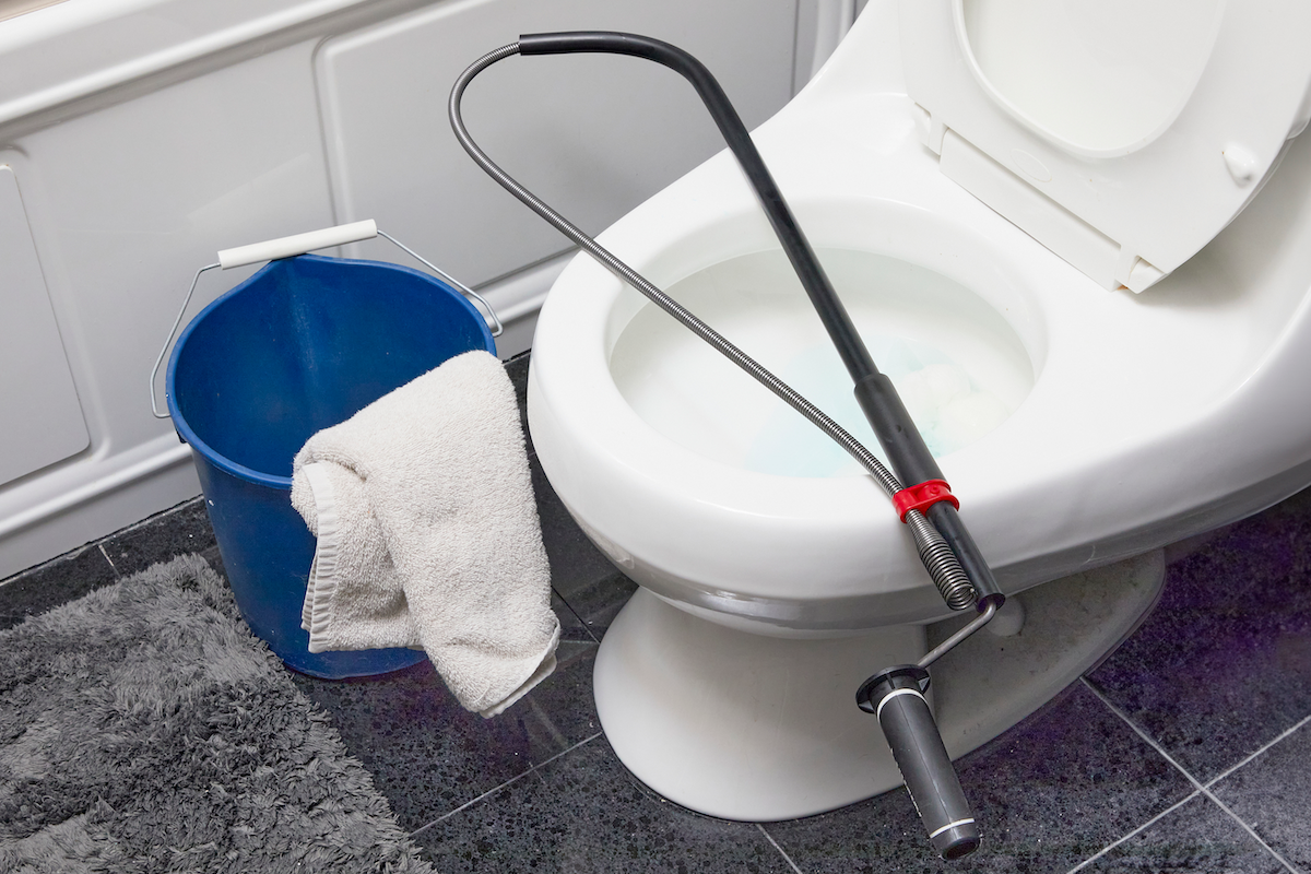 Toilet snake on top of a toilet with a bucket and clean towel nearby.