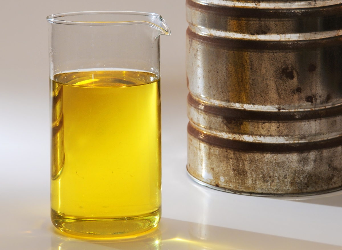 Gasoline in clear glass container with old gas can in background.